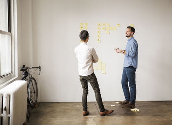 Business people discussing over sticky notes against white wall at creative office