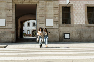 Female coworkers crossing street against building in city