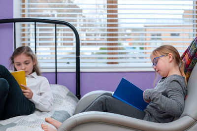 Two school age girlfriends sitting together in bedroom and doing school homework.