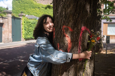 Portrait of smiling young woman against tree trunk