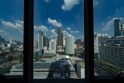 Buildings in city against sky seen through glass window