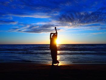 Silhouette woman standing at beach against sky during sunset