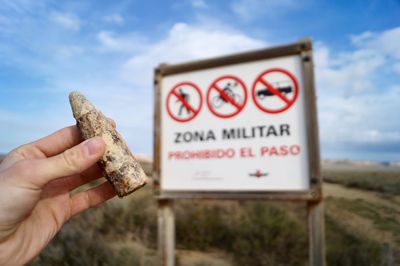 Close-up of hand holding object against information sign