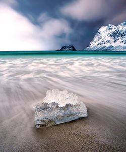 Ice on shore against cloudy sky