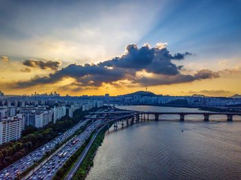 Bridge over river in city against sky during sunset