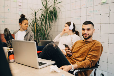 Portrait of smiling young businessman holding smart phone while sitting with female colleagues at small office