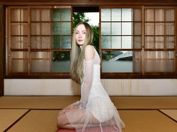 Portrait of a young woman standing against window