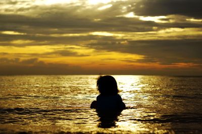 Silhouette woman in sea against sky during sunset