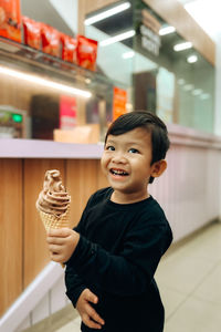 A boy holding ice cream with a happy smile in a cafe