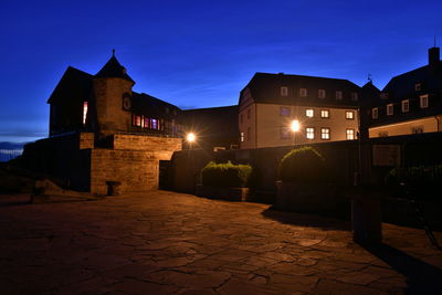 Illuminated street amidst buildings against sky at night