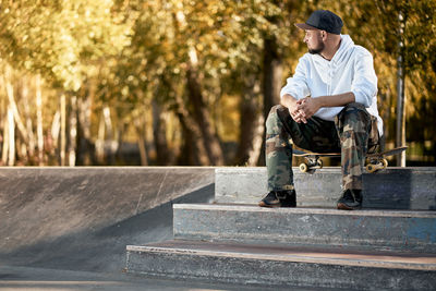 Man sitting with skateboard on staircase at park