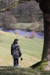 Rear view of woman standing by tree against river