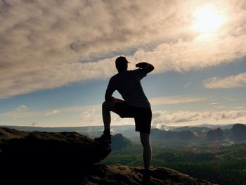 Rear view of man standing on rock against sky during sunset