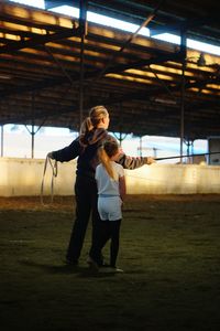 Rear view of woman with girl standing on field at animal pen