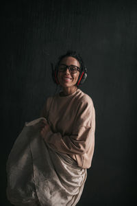 Portrait of smiling young woman standing against black wall