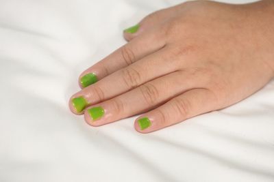 Cropped hand of woman with green painted fingernails on bed