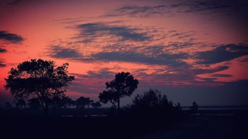 Silhouette trees on landscape against sky at sunset