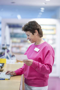 Smiling pharmacist using computer at desk in pharmacy store