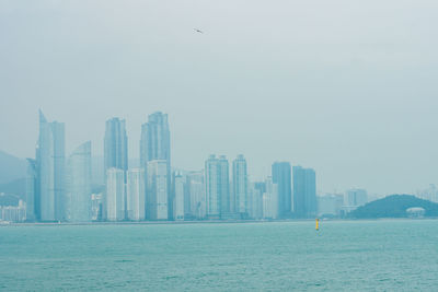 Modern cityscape by sea against sky