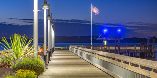Illuminated pier by sea against blue sky at night