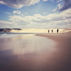 Friends walking at beach against cloudy sky