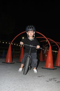 Portrait of boy riding push scooter on road at night