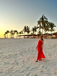 Rear view of woman standing at beach against clear sky during sunset