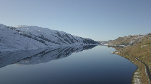 Scenic view of lake and snowcapped mountains against clear blue sky