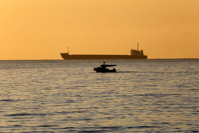 Silhouette boat sailing in sea against clear sky during sunset