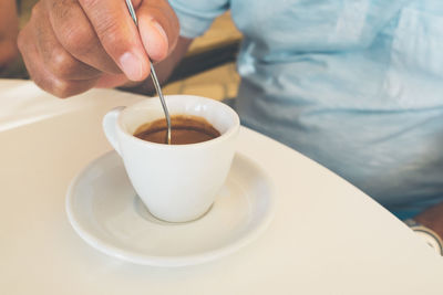 Cropped hand of woman stirring spoon in coffee on table