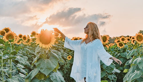 Young woman standing amidst sunflowers on agricultural field during sunset