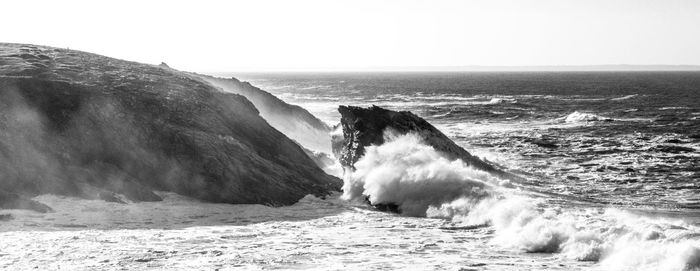 Scenic view of sea waves splashing on rocks against sky