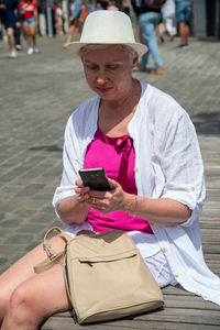 An aged caucasian woman in a hat and stylish summer clothes chats in a mobile