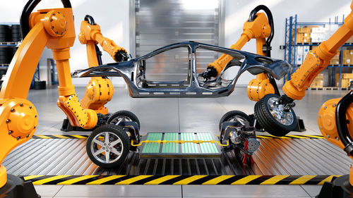 Assembly line in electric car factory with battery cells and industrial robotic arms, 3d rendering.