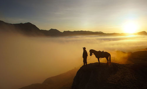 Silhouette man and horse on mountain cliff