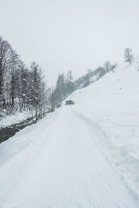 Snow covered road amidst trees against sky