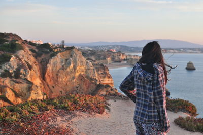 Rear view of woman standing on rock by sea against sky