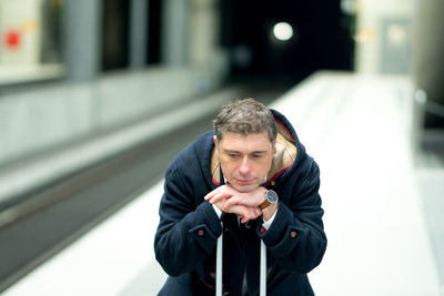 Man sitting on luggage at railroad station platform