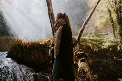 Side view of man standing on rock in forest