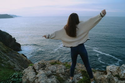 Rear view of woman standing at sea shore against sky