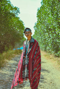 Portrait of young man standing with shawl on dirt road