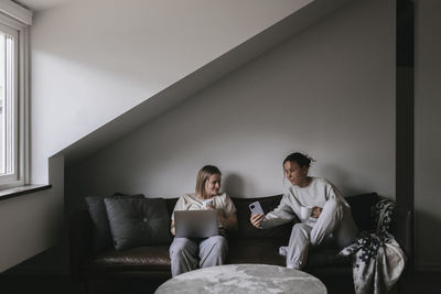 Homosexual couple sitting together on sofa and looking at cell phone