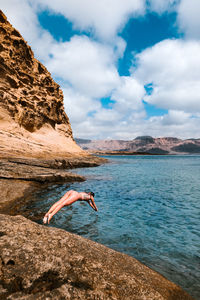 Man standing on rock by sea against sky