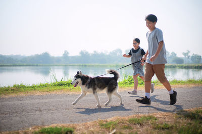Full length of children playing with their dog by the lake against sky