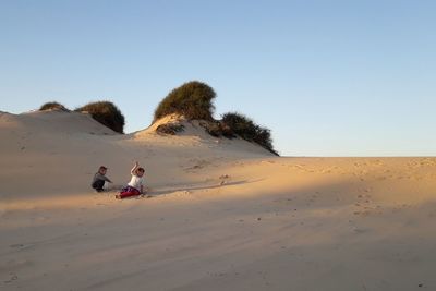 People on sand dune in desert against clear sky