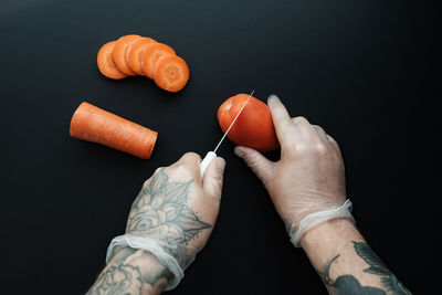 Cropped hand of woman holding red chili pepper against black background