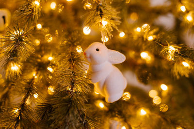 White bunny toy on a christmas tree with lights.