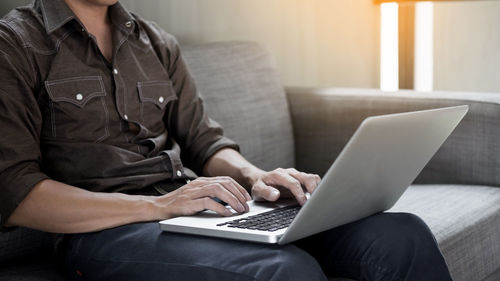 Midsection of man using mobile phone while sitting on sofa at home