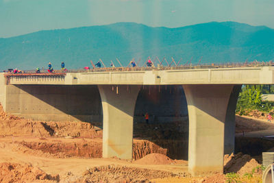 People on bridge over mountain against sky