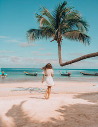 Full length of woman standing by palm tree on beach against sky